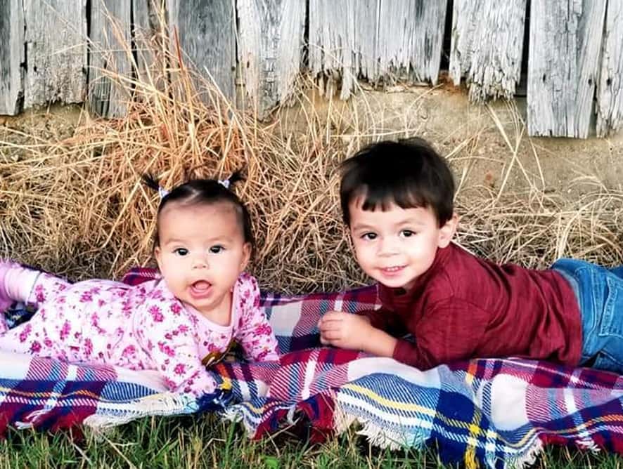 two young children and boy and girl sitting on grass by fence. - testimonial for Laura L.